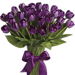 Bunch of purple tulips arranged in a clear glass vase with a purple ribbon bow