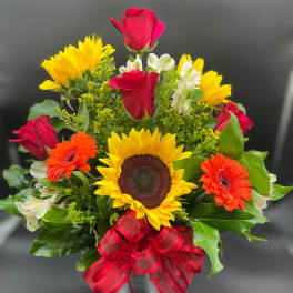 Bright mixed arrangement with sunflowers, red roses, orange gerberas and white blooms in a glass vase with red bow