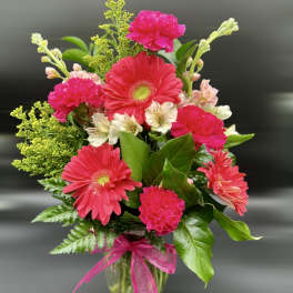 Bright pink gerbera daisies, carnations, and light alstroemeria in a clear vase with pink bow