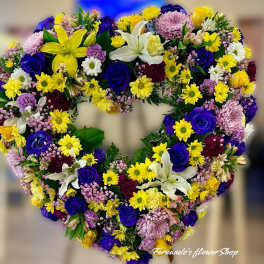 Heart-shaped sympathy wreath with yellow lilies, blue roses, daisies, and mixed flowers.