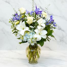 White lilies, cream roses, blue hydrangea, and purple flowers in a glass vase