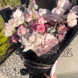 Hand-tied bouquet of pale pink roses and sweet peas wrapped in black paper with netted overlay