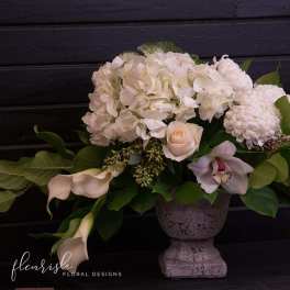 White floral arrangement in a gray pedestal vase with calla lilies and roses