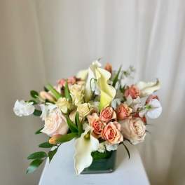 Arrangement of peach roses and white calla lilies in a square glass vase