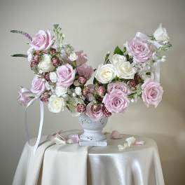 Asymmetrical arrangement of pink and white roses in a white urn on a draped table.
