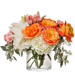 Bouquet of orange and pink roses with white lilies and hydrangeas in a clear glass vase
