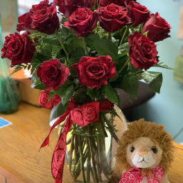 Red roses in a glass vase with a plush lion beside them
