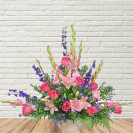 Pink roses and lilies arranged with purple accents in a clear vase.