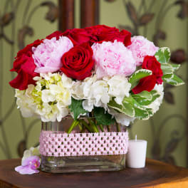 Red roses and pink peonies in a glass vase with a pink ribbon wrap