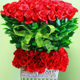 Tall arrangement of red roses with a green ribbon in a decorative pedestal vase