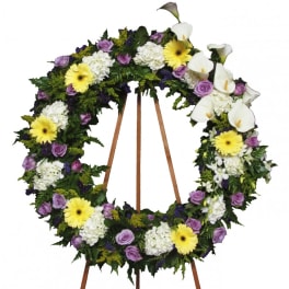 Large floral wreath with white calla lilies, yellow daisies, and purple roses on a stand