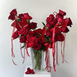 Tall arrangement of red roses with tropical red blooms and ribbons in a clear glass vase