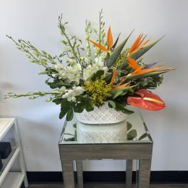 Tropical floral arrangement with white orchids and orange bird-of-paradise in a white vase