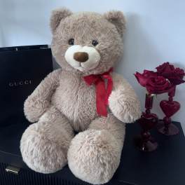 Teddy bear with a red ribbon beside a small vase of red roses
