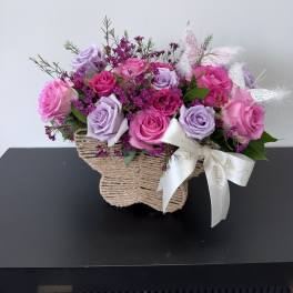 Pink and lavender roses in a woven basket with a ribbon bow