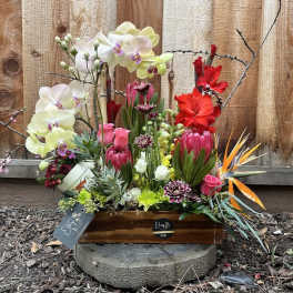 Mixed floral arrangement in a wooden box with orchids and bright tropical blooms
