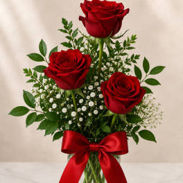 Three red roses in a glass vase with baby's breath and a red ribbon