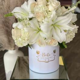 White lilies and cream roses arranged in a round white box