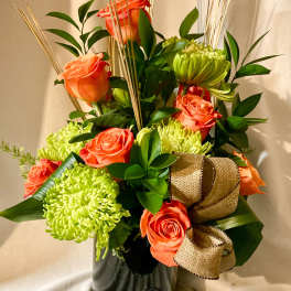 Orange roses and green chrysanthemums in a black vase with a gold ribbon
