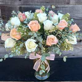 Bouquet of white and peach roses in a glass vase with a pink ribbon
