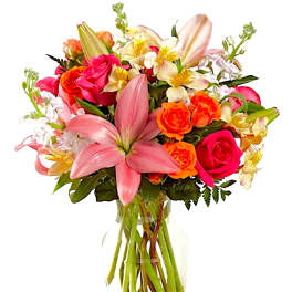 Mixed bouquet of pink lilies, roses, and orange blooms in a glass vase