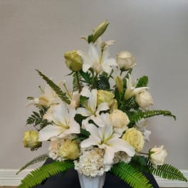 White lilies and cream roses arranged in a vase with fern accents