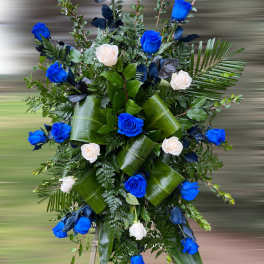 Standing spray of bright blue and white roses with large glossy green leaves on an easel