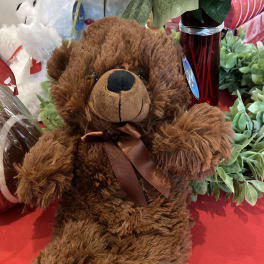 Brown teddy bear with a satin ribbon sitting among flowers