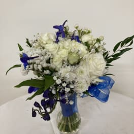 White and blue flower bouquet in a glass vase with a blue ribbon