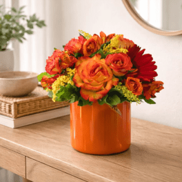 Compact bouquet of orange and red roses with yellow accents in an orange vase