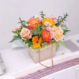 Mixed bouquet of peach, pink, and orange flowers in a beige gift box