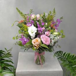 Mixed bouquet of pink, white, and peach flowers in a glass vase with a pink ribbon
