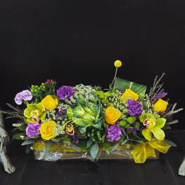 Bright yellow and purple floral arrangement in a low rectangular container