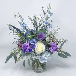Mixed bouquet in a clear glass vase with blue, purple, and white flowers