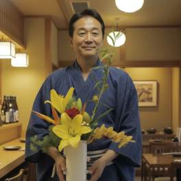 Man in a blue kimono holding a white vase of yellow and red flowers