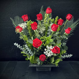 Red roses arranged in a low black container with greenery