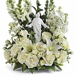 All-white arrangement of roses, lilies, and snapdragons surrounding a white Jesus figurine