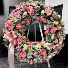 Large pink and white floral wreath with roses, lilies, and gerberas on an easel