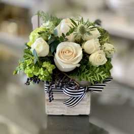 White roses and green flowers arranged in a small wooden box with a striped ribbon