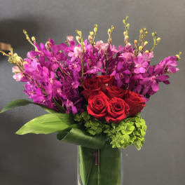 Red roses and purple orchids in a clear glass vase