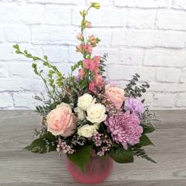 Pink and white roses with purple blooms in a pink vase