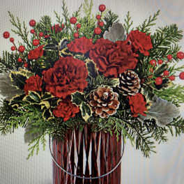 Red carnations and pinecones in a glass vase with evergreen sprigs