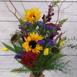 Mixed bouquet with sunflowers, tulips, and red blooms in a glass vase
