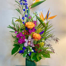 Tropical bouquet with orange bird-of-paradise and mixed blooms in a glass vase