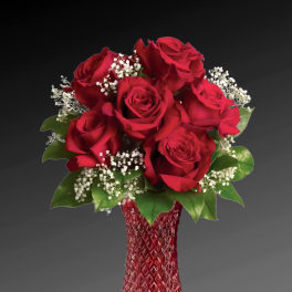 Red roses arranged in a red glass vase with white filler flowers