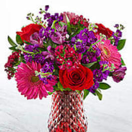 Mixed bouquet of red, pink, and purple flowers in a glass vase