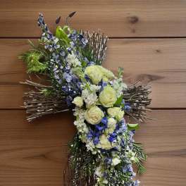 Cross-shaped floral tribute with white and blue flowers on a twig base