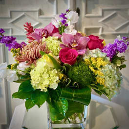Colorful mixed bouquet in a clear glass vase with roses and orchids
