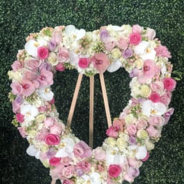 Heart-shaped floral wreath of pink, white, and lavender blooms on a wooden stand