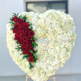 Heart-shaped white floral arrangement with a red rose cascade
